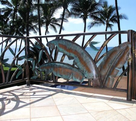 Rustic metal gate with artistic fish design near palm trees.
