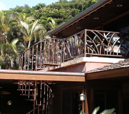 Spiral staircase leading to a balcony with wooden railing surrounded by greenery.
