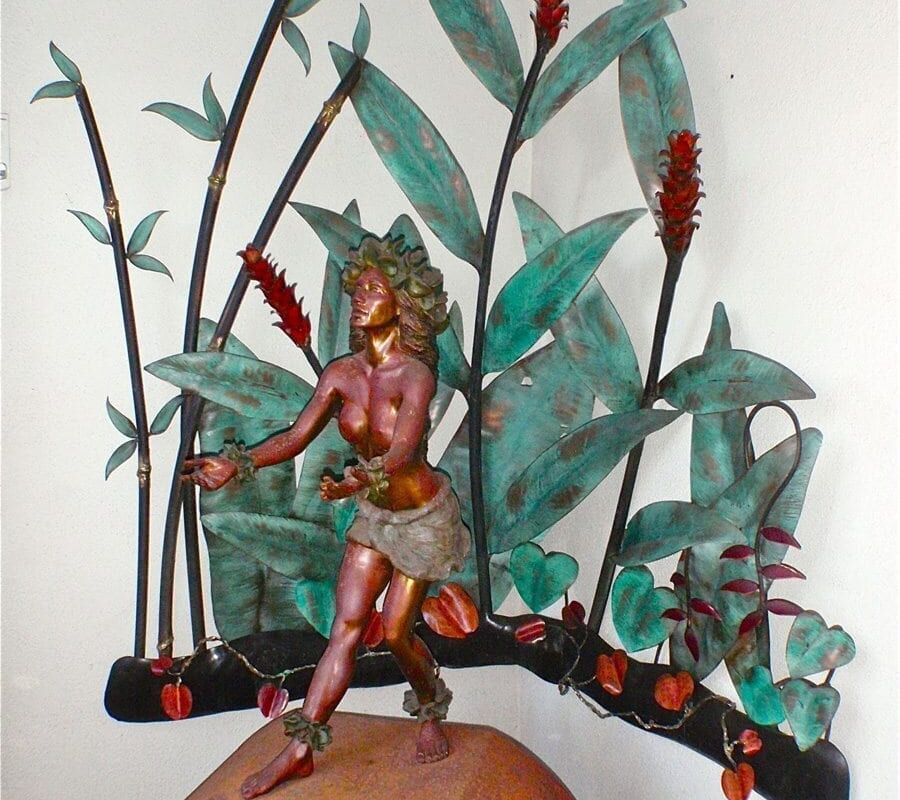 Intricate metal sculpture of a dancing figure with a leafy backdrop.