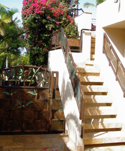 Sunlit outdoor staircase with white walls and a wooden gate beneath flowering plants.