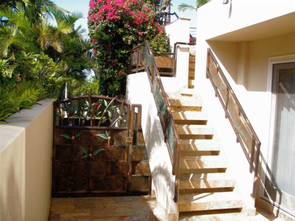 Sunny outdoor staircase with flowering plants and wooden railing.