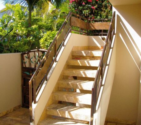 Sunlit outdoor staircase with stainless steel railings and beige tiles.