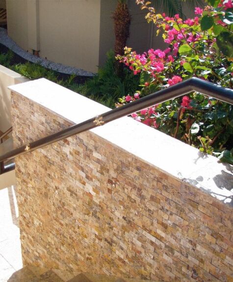 Stone wall with metal handrail beside a stairway in a garden.