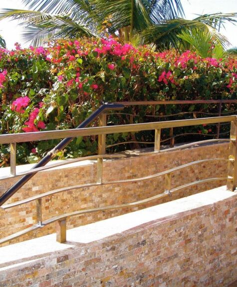 Stone pathway with a wooden handrail and vibrant flowering bushes.