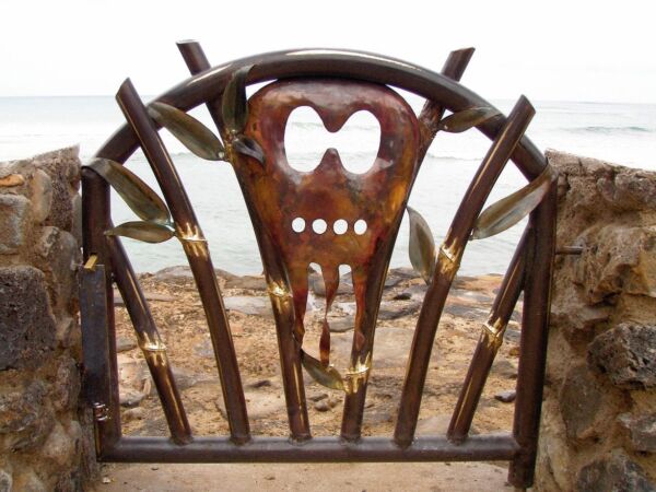 Rusty metal gate with a skull design in a barren outdoor area.