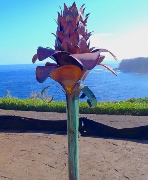 A decorative metal flower sculpture near a beach with ocean in the background.