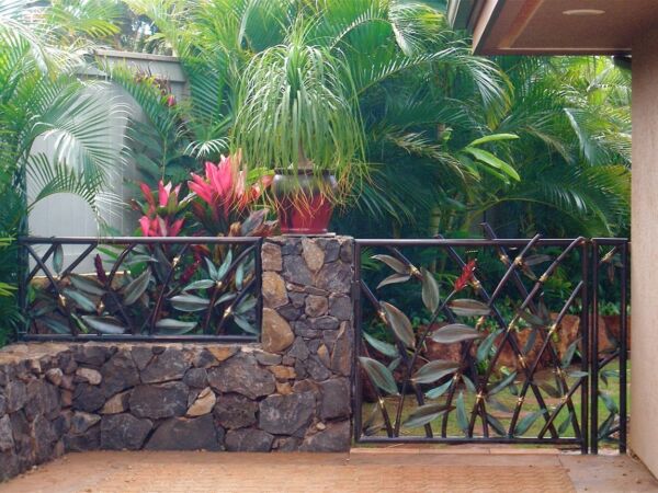 Lush tropical garden with vibrant plants behind stone and metal fence.