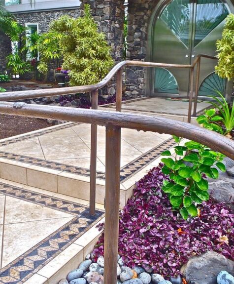 Rustic wooden handrail along garden pathway with greenery and stones.