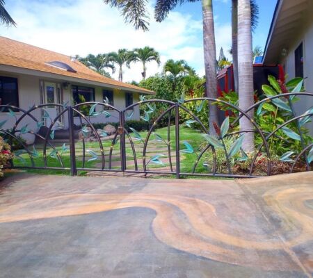 Decorative metal fence with a garden and houses in the background.