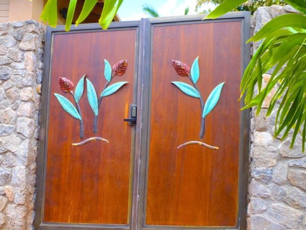 Wooden double gate with leaf designs framed by stone walls and greenery.