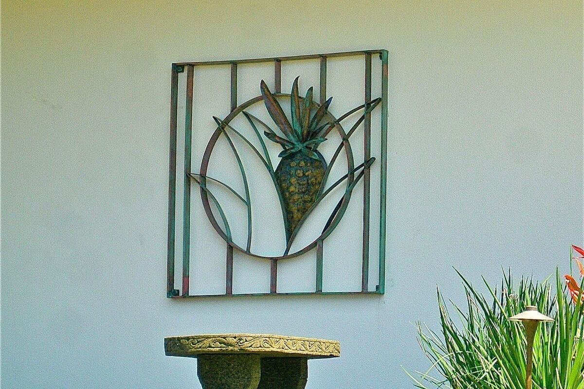 Decorative metal pineapple art mounted on a yellow wall above a stone bench.