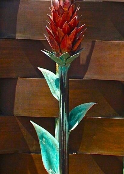 Decorative metal sculpture of a tall red flower with green leaves.