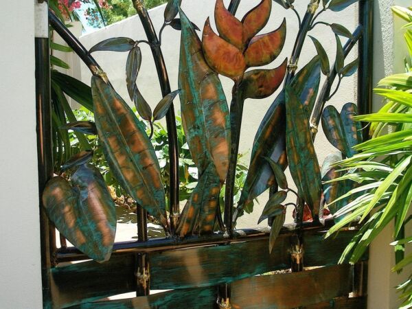 Decorative metal gate with leaf patterns and glass panels in a garden.