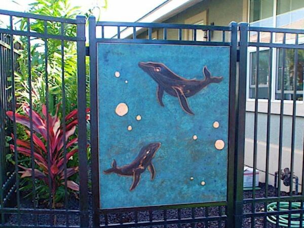 Metal fence panel with bird and fish designs in a garden setting.
