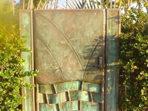 Intricately designed metal door set in a lush garden with palm trees.