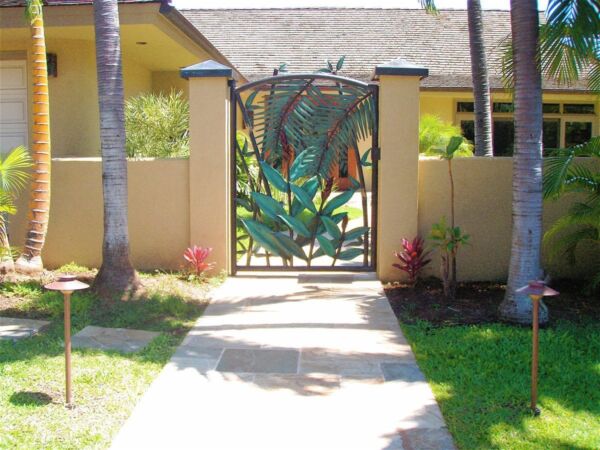 Decorative metal gate with floral design at a garden entrance.
