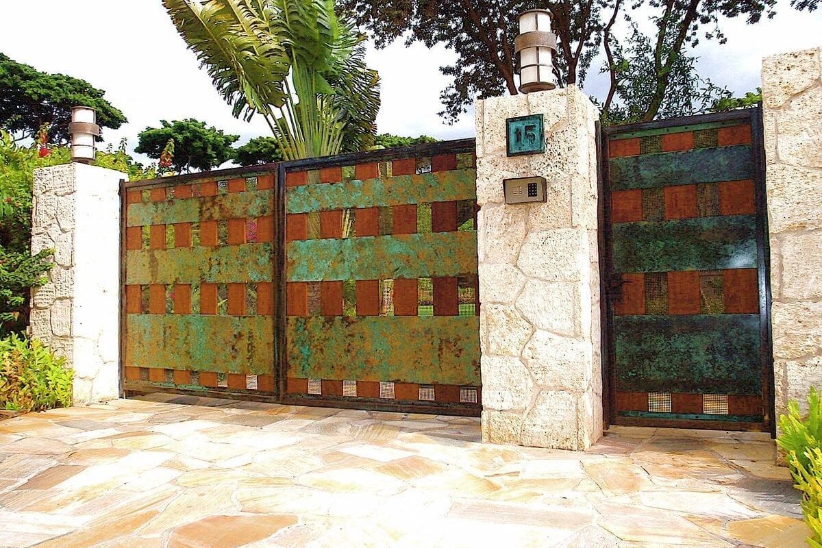 Rusty metal gate with stone pillar and house number.