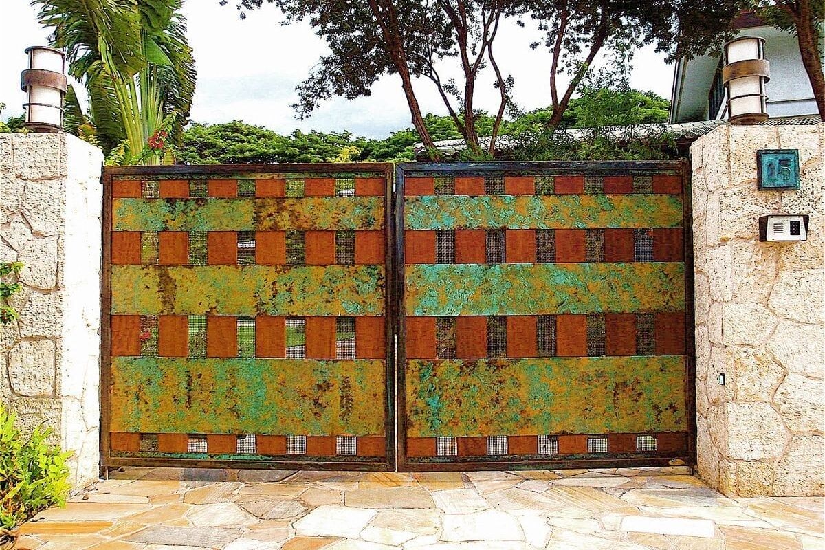 Rusty metal gate with green and orange patches in a garden setting.