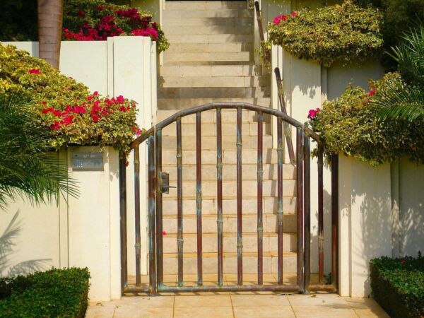 A black metal gate in front of garden stairs with flowers.