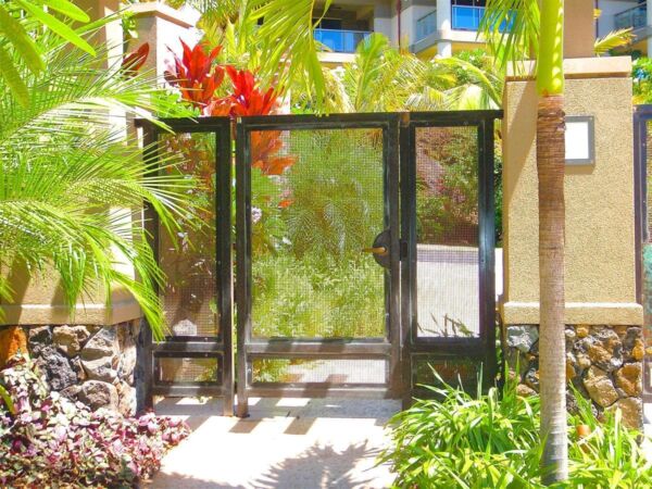 A black metal garden gate surrounded by lush green plants and colorful flowers.