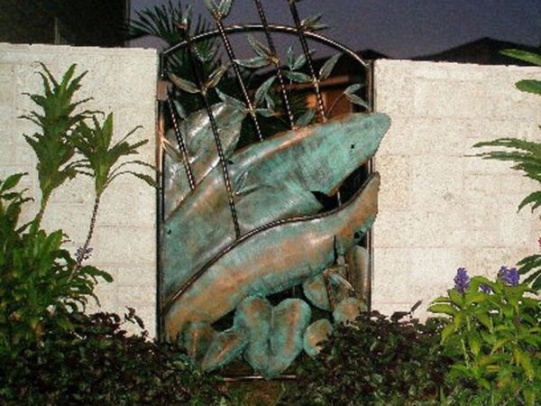 Outdoor fish sculpture integrated into a wall at night.