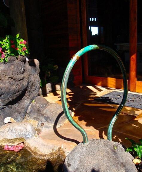 A green snake sculpture near rocks and flowers in a garden setting.
