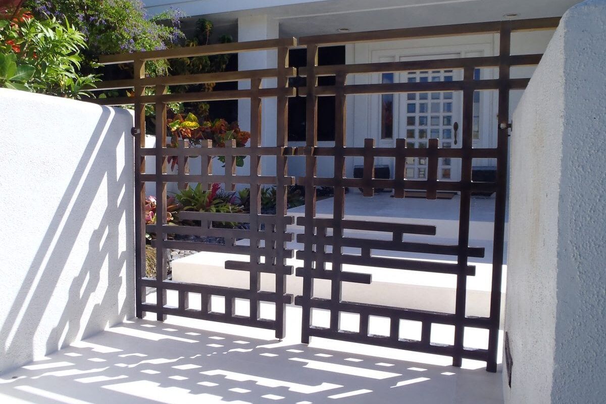 Modern metal gate with geometric design at a house entrance.