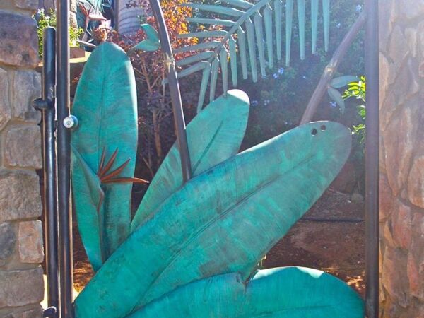 Decorative metal gate with teal leaf designs and a person behind it.