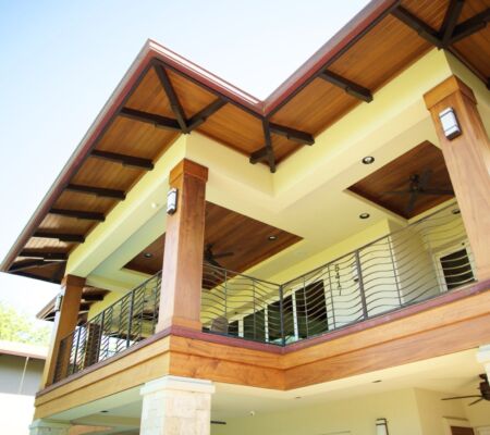 Modern house balcony with wooden beams and glass railings under a clear sky.