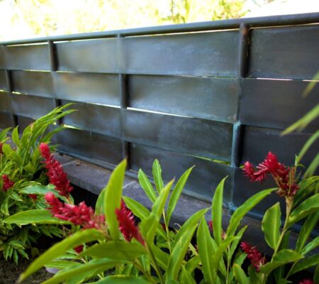 Metal wall paneling with plants and red flowers in front.