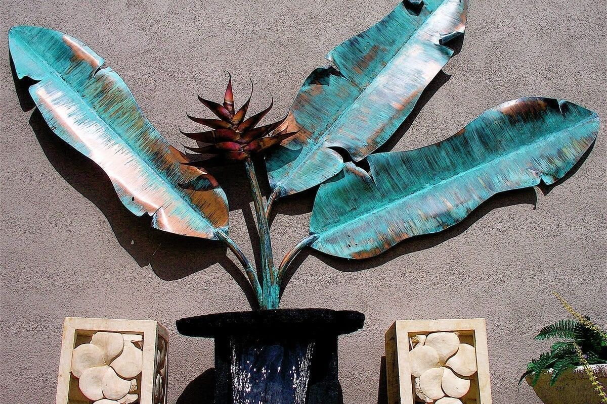 Decorative metal sculpture resembling a plant with broad leaves in a black pot.