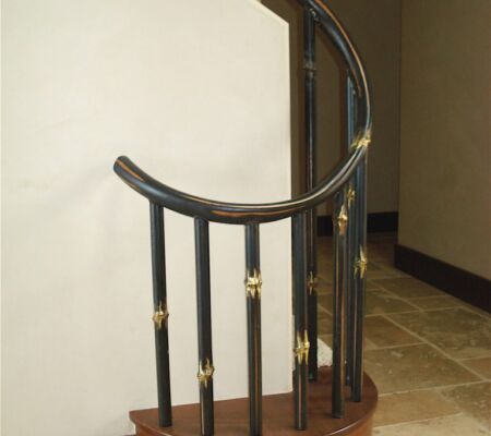 Curved wooden handrail with black and gold balusters.