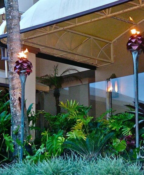 Tiki torches lit in a garden beside a covered patio area at dusk.