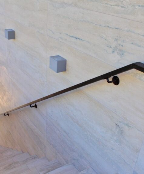 Minimalist staircase with a sleek black handrail and marble walls.