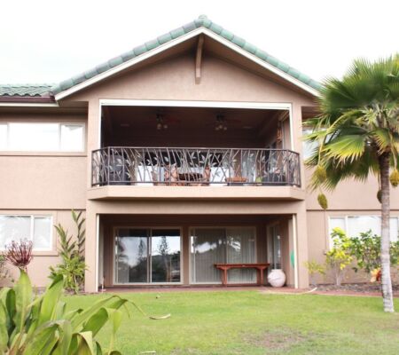 Two-story house with balcony and patio in a lush garden.