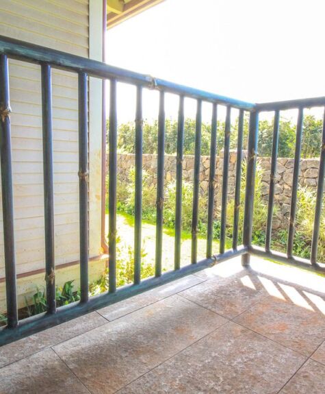 Empty balcony with black metal railing overlooking greenery.