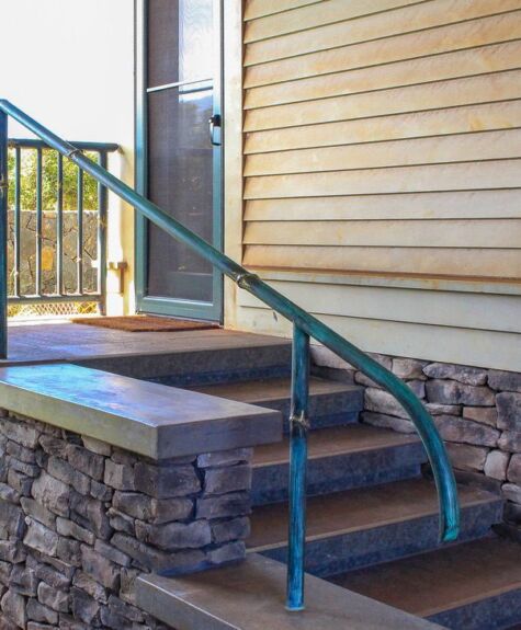 Curved metal handrail beside stone steps leading to a wooden porch.