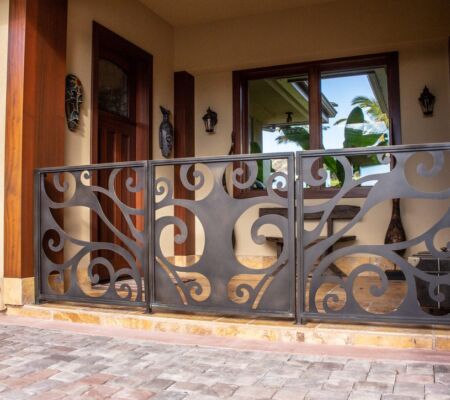 Ornate metal gate with swirling patterns and a brick driveway.