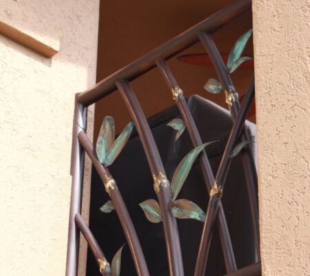 Decorative metal balcony railing with leaf motifs on a beige building.