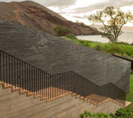 Modern outdoor staircase with dark stone steps and metal railing beside a scenic hillside.