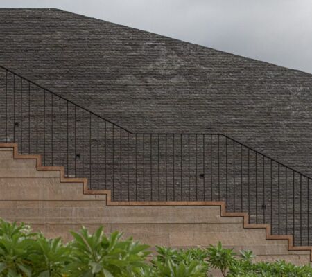 Stone staircase with a black iron railing against a large stone wall.