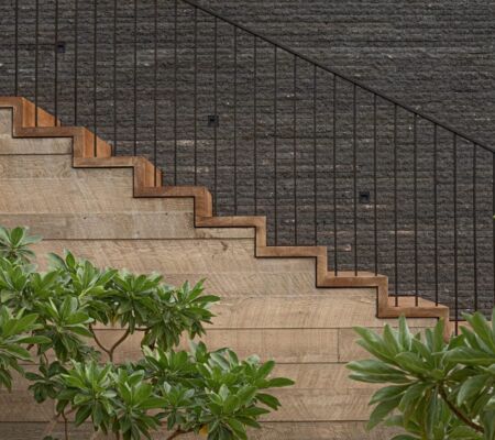 Modern staircase with stone steps and metal railing against a dark brick wall.