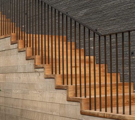 Wooden staircase with black metal railings against a stone wall.