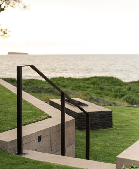 Modern outdoor seating area overlooking the ocean with stone steps and grassy patches.