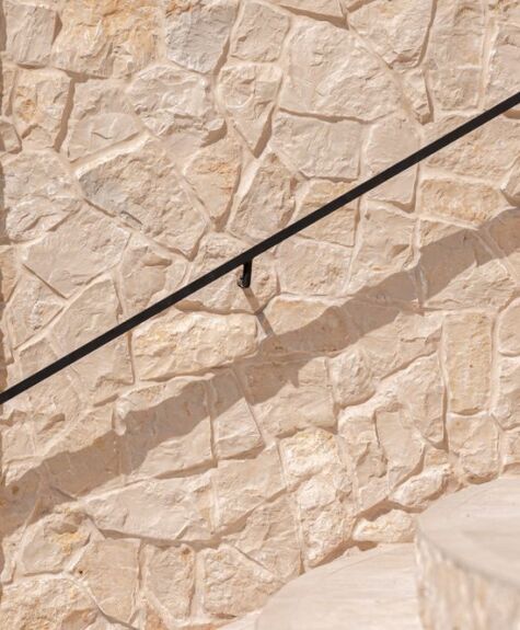 Stone staircase with a black metal handrail casting a shadow.