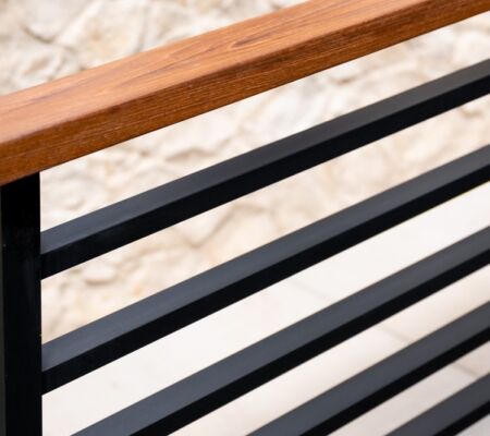 Close-up of a modern railing with wooden handrail and black metal bars.