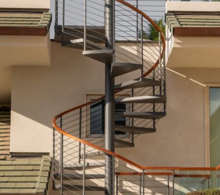 A modern spiral staircase with metal railings on a building exterior.