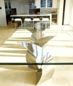 Modern glass table with a reflective, metallic base in a bright room.