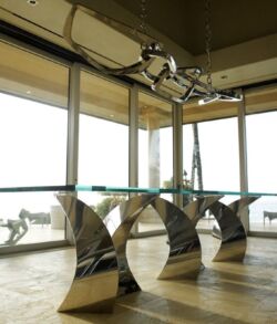 Modern glass conference table with unique curved metal legs in a bright office.