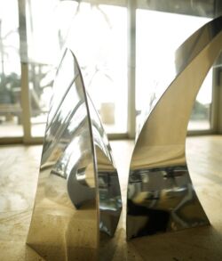 Modern metallic sculpture with abstract, curved shapes on a wooden floor.